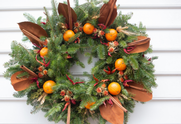 Green circle wwreath with orange leaves and oranges and red peppers around it.